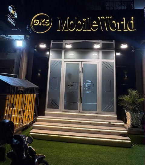 La devanture de GKS Mobile World le soir : enseigne dorée allumée, double porte vitrée et marches éclairées